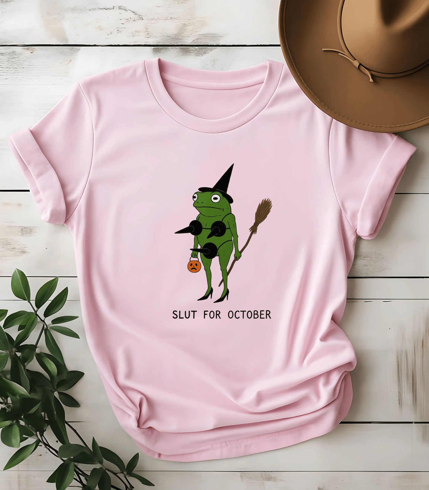 Pink graphic tee with witch frog holding broom and pumpkin, text 'SLUT FOR OCTOBER'