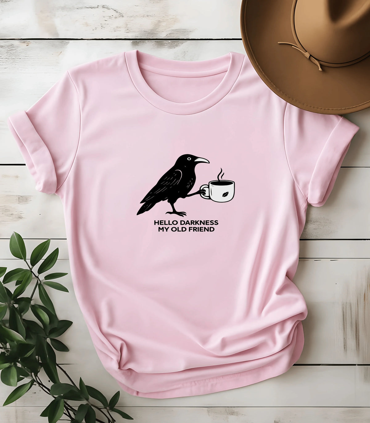 Pink graphic tee with crow holding coffee cup, text 'Hello Darkness My Old Friend'