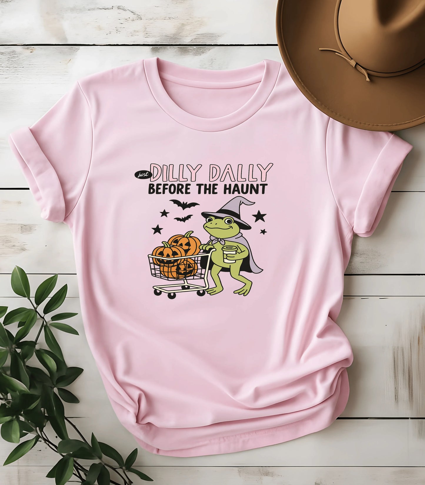 Pink t-shirt with frog in witch hat pushing pumpkin cart, text 'Just Dilly Dally Before the Haunt'