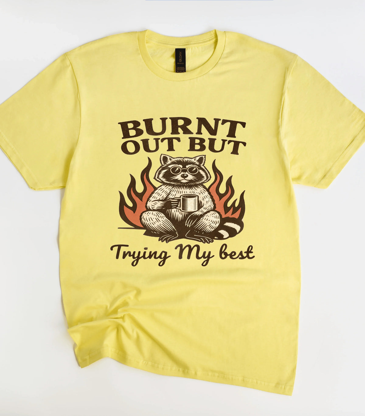 Funny raccoon graphic tee with 'Burnt Out But Trying My Best' text on yellow shirt