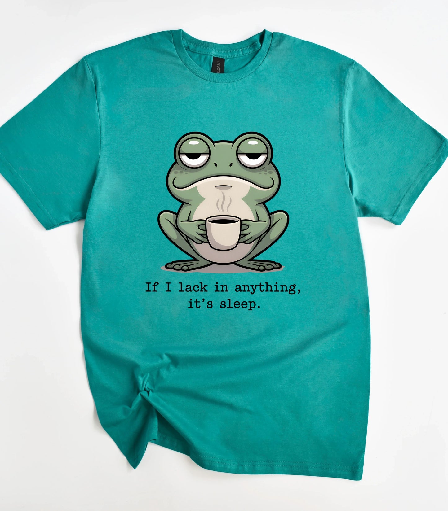 Sleepy frog holding coffee cup graphic t-shirt with text 'If I lack in anything, it's sleep.'