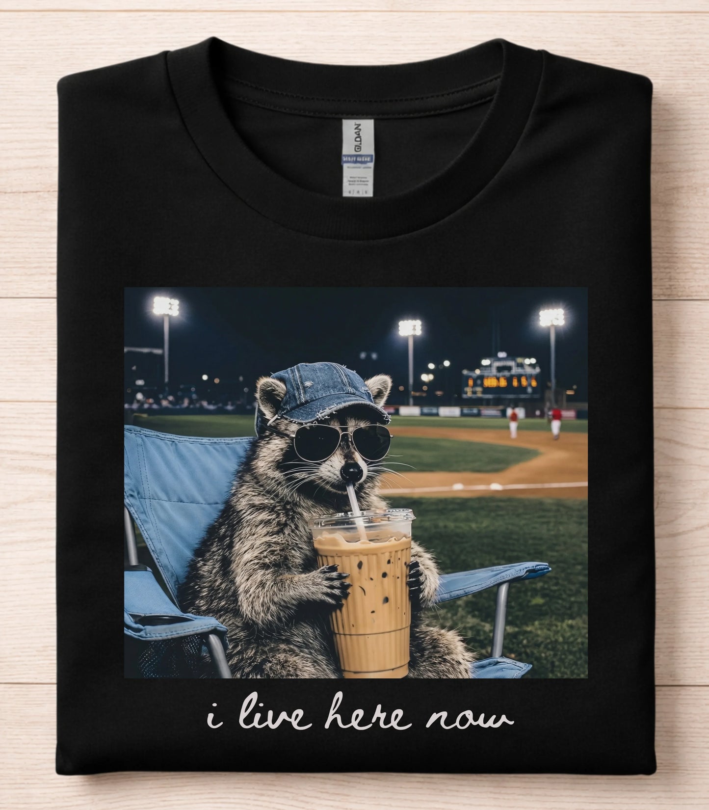 Funny raccoon graphic tee with sunglasses and iced coffee at baseball game