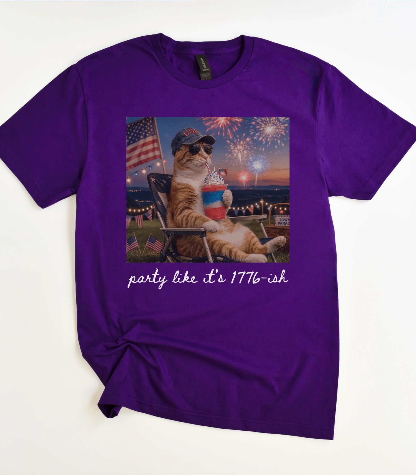Funny cat graphic tee with patriotic cat sipping slushie, fireworks, and 'party like it's 1776-ish' text on purple shirt